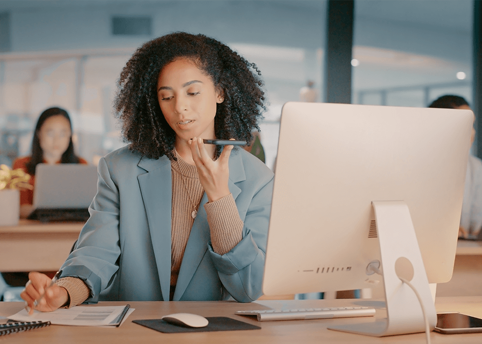 AI_in_workplace Woman in office talking to smartphone at desk
