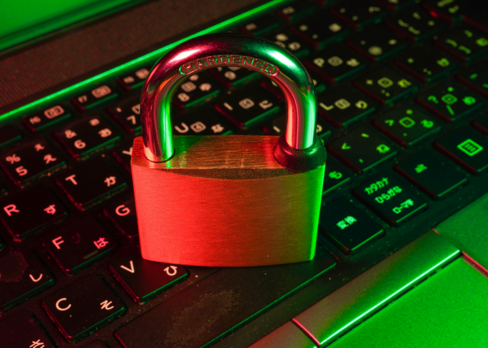 Close-up of a metal padlock resting on a laptop keyboard under red and green lighting, symbolising cybersecurity and data protection for networked systems.