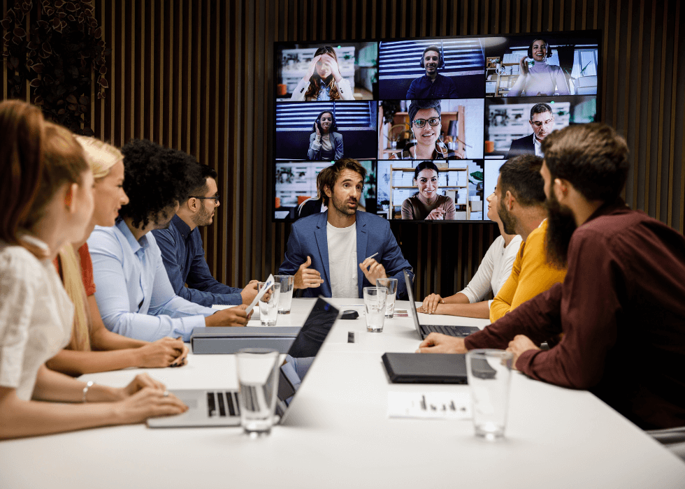 teams_vs_zoom Young manager sitting at a conference table and leading a meeting with a group of his employees